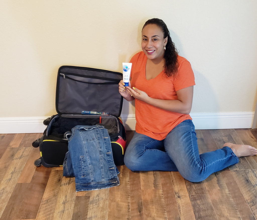 Woman holding toothpaste next to a suit case